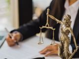 Photo of lawyer writing documents with Lady Justice statue in forefront