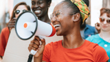 Photo focused on a young woman, smiling, with a megaphone.
