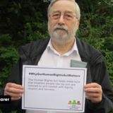 Image of man holding up sign saying "#WhyOurHumanRightsActMatters The Human Rights Act helps make sure that disabled people like my son are listened to and treated with dignity, respect and fairness"