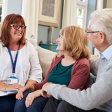 An older woman and man, sitting on a sofa, talking with a support worker.