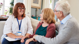 An older woman and man, sitting on a sofa, talking with a support worker.