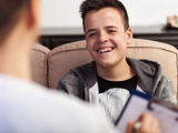 Photo focused on a young man, smiling, speaking with a health worker, who is blurred with back to the viewer