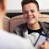 Photo focused on a young man, smiling, speaking with a health worker, who is blurred with back to the viewer