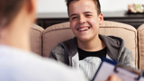 Photo focused on a young man, smiling, speaking with a health worker, who is blurred with back to the viewer