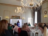 Woman stood at front of room full of people leading a presentation