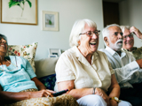 Group of older people sat together on a sofa, leaning forward and laughing.