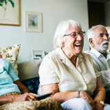 Group of older people sat together on a sofa, leaning forward and laughing.