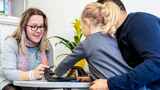 Photo of a support worker, looking at items on a desk with a child and her father.
