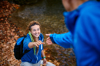 Photo focused on a young woman, smiling, outdoors walking up an incline, hand outstretched to a man reaching for her hand. He is blurred with his back to the viewer.