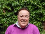 Photo of man in pink jumper sitting outside and smiling