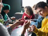 Photo of a group of people with learning disabilities doing arts and crafts projects, focused in on a young man, smiling.