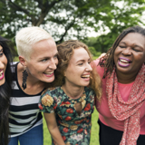 Photo of a diverse group of women smiling, with their arms around shoulders, focused on their faces. 