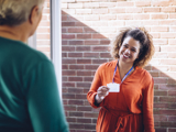 Photo of a social worker at a woman's front door, showing her identity badge, smiling