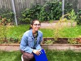 Photo of woman in denim jacket and glasses crouched outside in garden