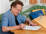 Photo of an older woman sat at a table signing a will.