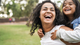 A woman giving a piggyback to a child, both smiling.