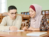 Two young adults sat at a table looking over papers.